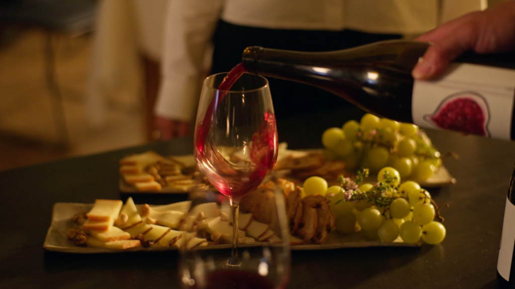 Copa de vino tinto sirviéndose junto a una tabla de quesos y uvas