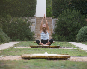Mujer haciendo yoga con los brazos elevados en el jardín del Hostal Empúries