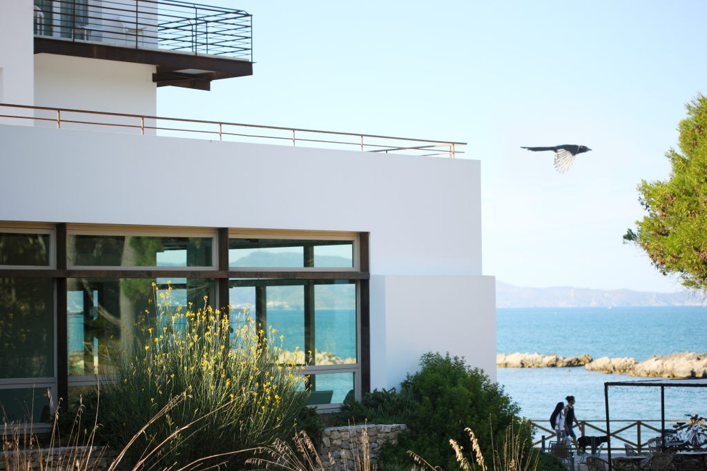 Fachada del Hostal Empúries junto al mar con un pájaro volando